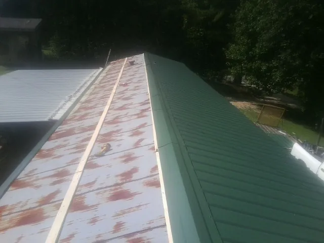 Old rusted panels beside newly installed green metal roofing — Wind Damage Roof Repair by Roofing Brothers in Newark