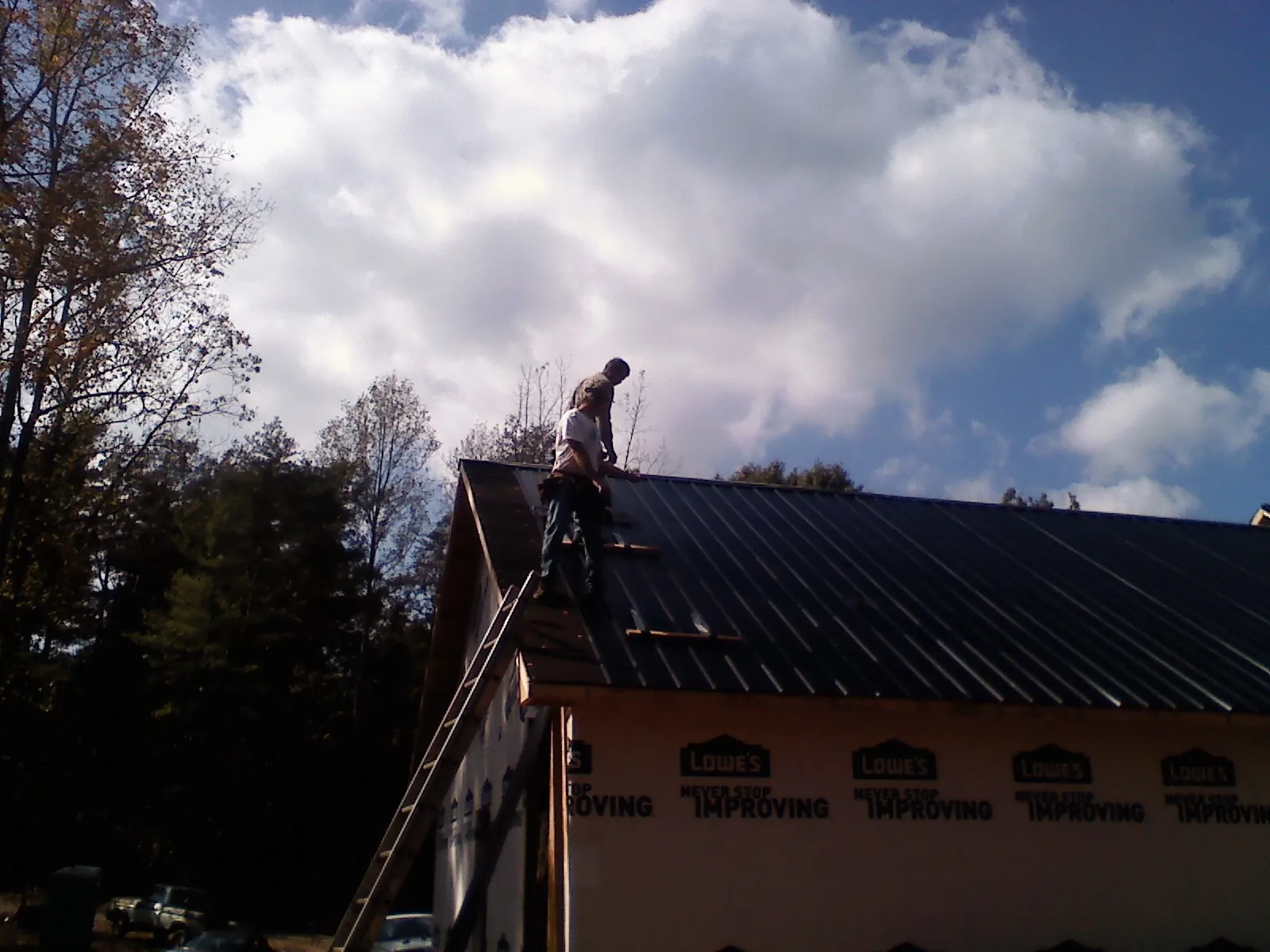 Roofer fastening dark metal panels high against a cloudy sky in Newark